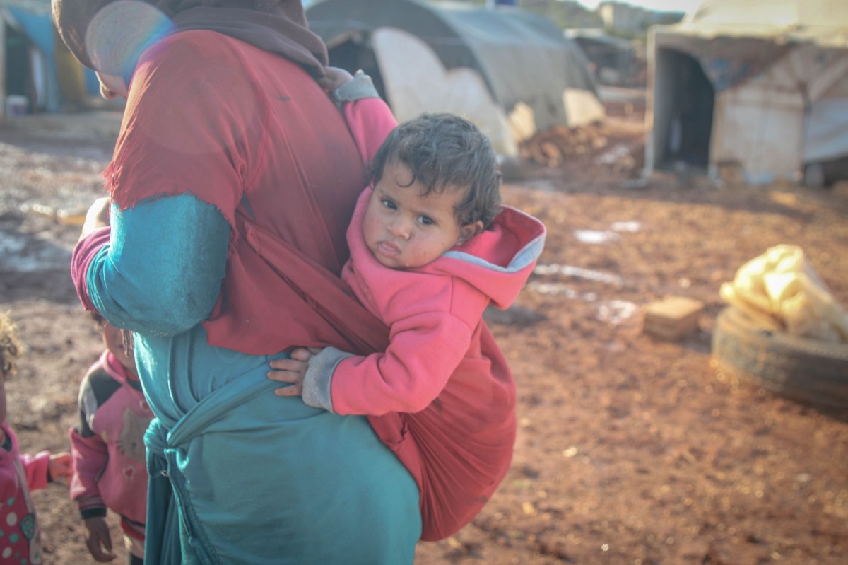 Refugee family in Seueta, Spain, with a child holding a sign in Spanish and English about the refugee crisis and social reaction.